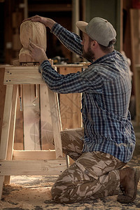 身着工作服的建筑工人锯在车间里用木头雕刻出一个男人的头图片