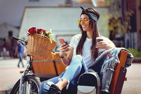使用智能手机和喝咖啡的骑自行车带花篮图片