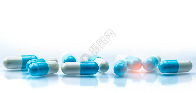 蓝色和白色胶囊药丸散布在白色背景上图片