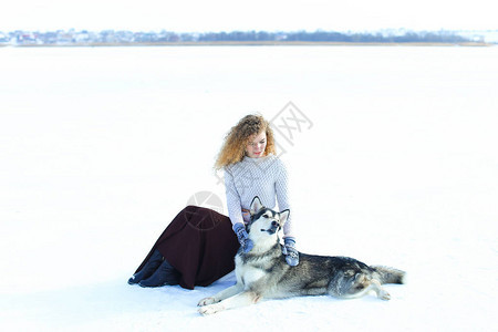 穿着毛衣棕裙子和手套的女孩坐在雪上图片