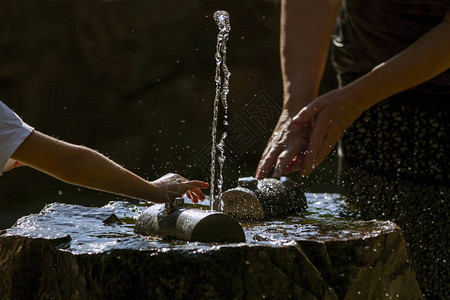 手和新鲜的冷的可饮用的水源在炎热和阳光明媚的夏日喝水未受污染的天图片