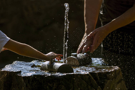 手和新鲜的冷的可饮用的水源在炎热和阳光明媚的夏日喝水未受污染的天背景图片