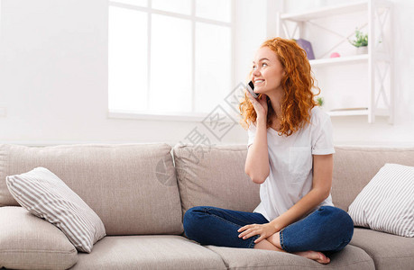 与朋友愉快的交谈有吸引力的微笑年轻红发女人坐在家里的米色沙发上谈手机技术通图片