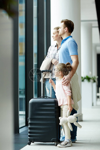 持行李旅行者家属在机场出港时通过透明门看望的托图片