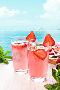 一杯草莓柠檬水木桌上的莫吉托鸡尾酒夏日海背景图片