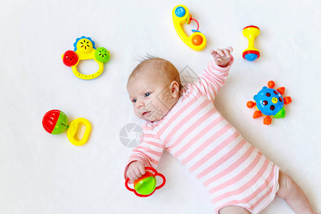 可爱的新生婴儿在白色背景上玩很多五颜六色的拨浪鼓玩具图片