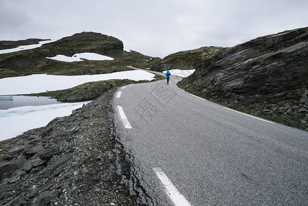 挪威人与穿着蓝色夹克的人在山上的景色在白雪皑的道路bjorgavegen图片