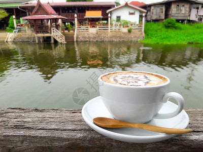 河边木桌上的热拿铁咖啡杯图片