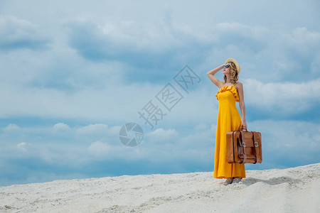 穿着黄色洋装在沙滩上放手提箱的年轻女子图片