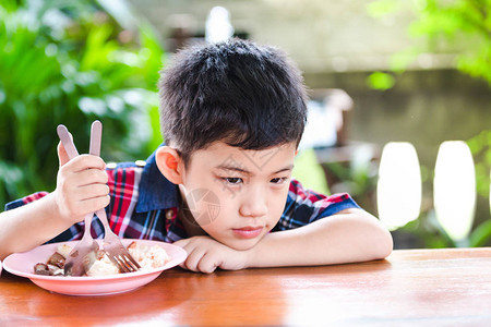 亚洲小男孩在木制桌上吃着米饭吃着无聊图片