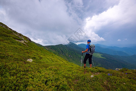 冒险家正在低云下沿着绿色山脊行走在暴风雨前的山上图片