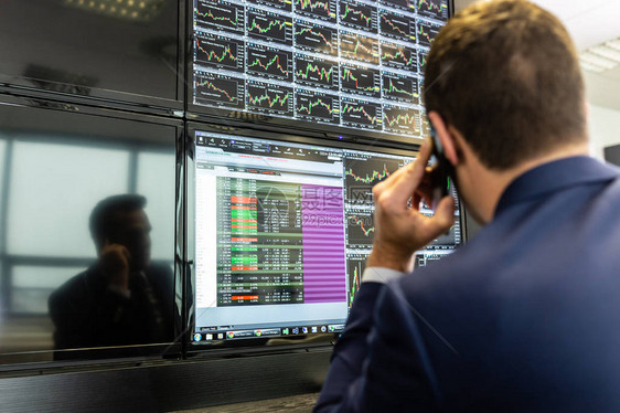 用手机交易股票的商人股票分析师在多个计算机屏幕上查看图表索引和数字股票交易员评估经济数据蓝色图片