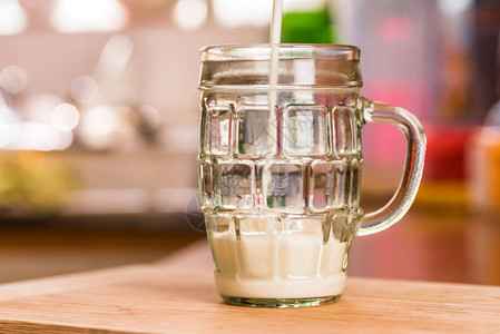 在厨房桌子上倒满四分之一整杯干净的玻璃杯时将新鲜的Kefirprobiotik饮料倒在图片
