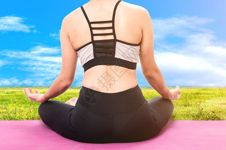 在蓝天背景的绿草上练习瑜伽的女人图片