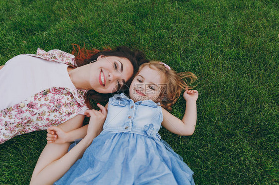 穿着轻便连衣裙的微笑快乐的女人和可爱的小女孩躺在公园休息的绿草上图片