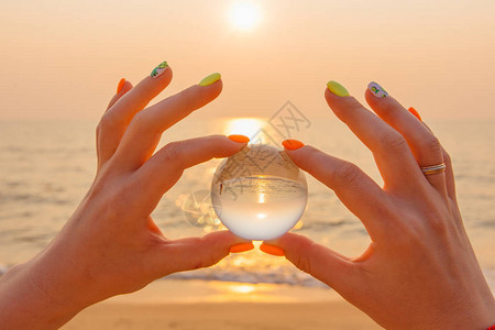 水晶透镜球在手在海滩上反射大海和日落图片