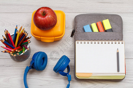 耳机彩色铅笔黄色午餐盒苹果和开放式练习本放在袋子铅笔盒上图片