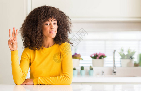 身穿黄色毛衣的非洲裔美国妇女在厨房展示并用三号手指向上指着图片