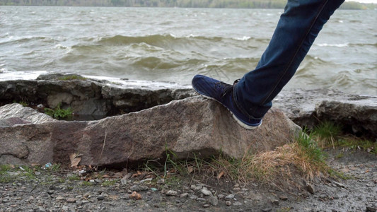 男人的腿站在湖前的一块石头上水淹没的石头关闭在河边放松的男脚在湖岸边图片