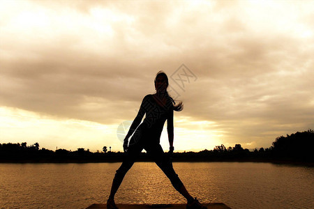 黄昏天空背景下日落时分在海滩上练习瑜伽的女士的黑暗剪影图片