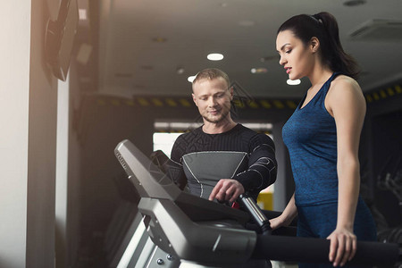 健身教练在椭圆机上帮助年轻女子教练在跑步机上与女孩讨论锻炼计划健身房的有氧运动健康的生活方背景图片