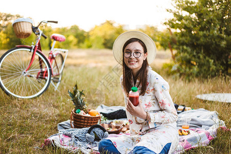 戴着眼镜和帽子的漂亮微笑女孩坐在野餐毯上图片