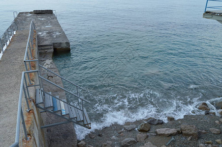 从码头到大海的金属楼梯波浪冲入岩石中图片