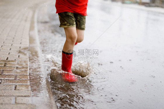 穿着红色雨靴的孩子跳进水坑特写孩子玩得开心泼水温暖的夏雨图片