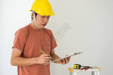 戴黄色头盔的年轻建筑师工程师的肖像在纸上写下新房子室内设计的划为现代空白建造的家具或橱柜图片