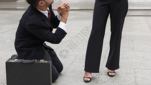 悲伤的商人在办公楼外没有得到晋升或受到惩罚后跪下举手请求同情背景图片