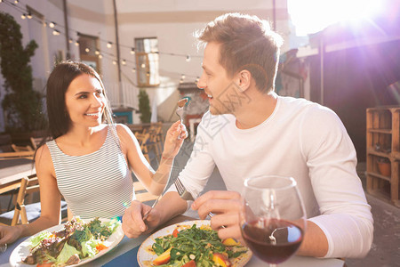 快乐的女人开心的女士给男朋友吃肉而他们一起吃美味的晚餐时图片