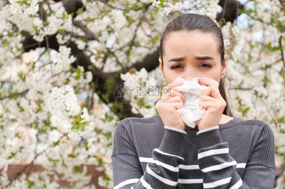 在开花树附近擦鼻毛的年轻女图片