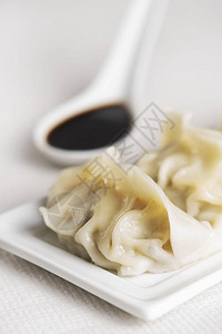 一些亚洲饺子或饺子在白色陶瓷盘和白色陶瓷勺形酱油碗上的特写背景图片