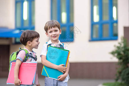 可爱的小学生在校园里轻快地交谈孩子们的心情很好温暖的春天早晨在同学的书包背后在其中一个男孩鲜红色背景图片