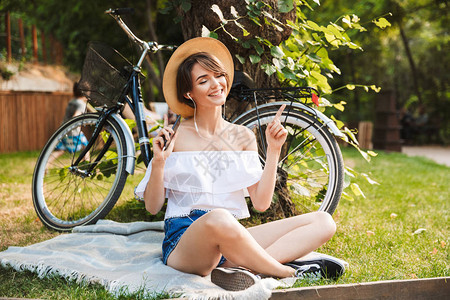 微笑的小女孩坐在公园里骑着自行车用手机图片