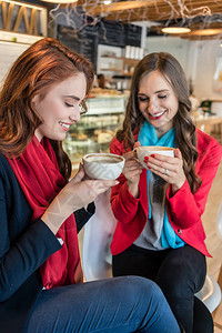 两位年轻美女在时尚咖啡店一起喝美味热巧克力时做白图片
