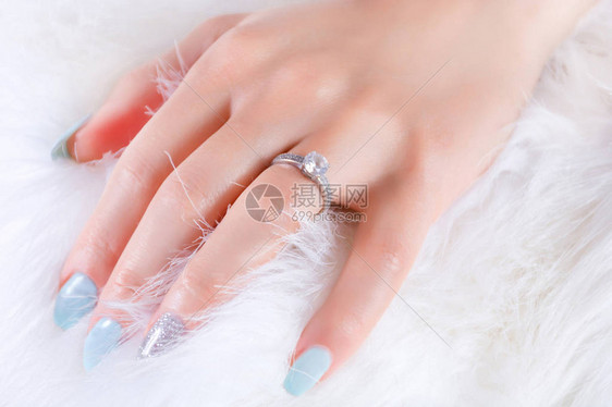女手与钻石订婚戒结婚戒指和白毛皮背景上的蓝指甲油美化和珠宝概念关闭图片