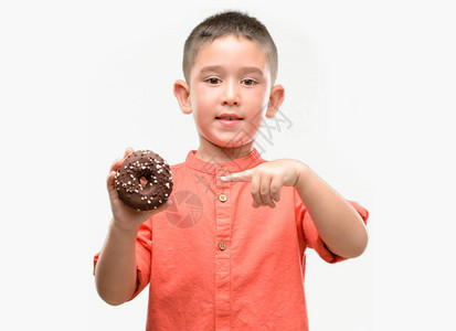 黑头发的小孩吃甜圈很高兴用手和指点图片