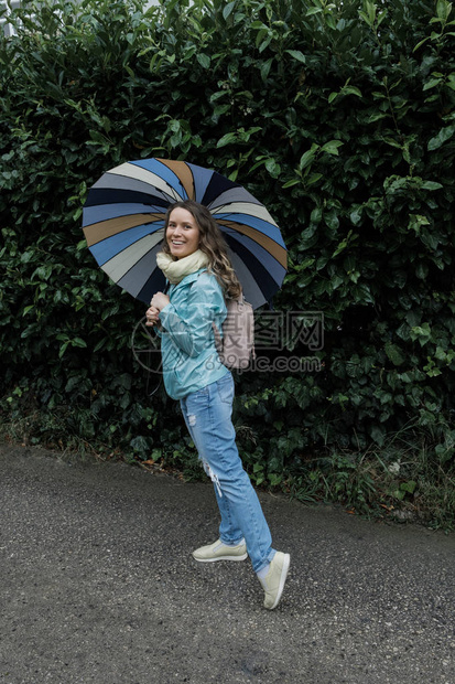 秋天或春天在公园的雨中微笑的金发女郎图片