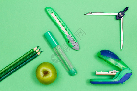 彩色铅笔苹果触摸尖笔纸刀指南针和绿背景的订书机图片