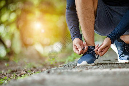 男子系慢跑鞋一个人在阳光明媚的日子在户外跑步关注两只手伸向鞋的侧面年轻的男慢跑员在户图片