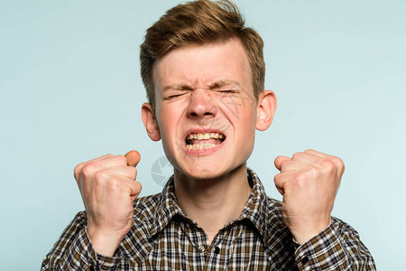 愤怒和仇恨被激怒的男人呲牙咧嘴一个年轻人在浅色背景上的肖像情感