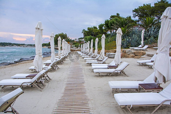 希腊沙滩上美丽的日落海滩和悬崖上有封闭的太阳雨伞和防晒床展望夏季场景图片