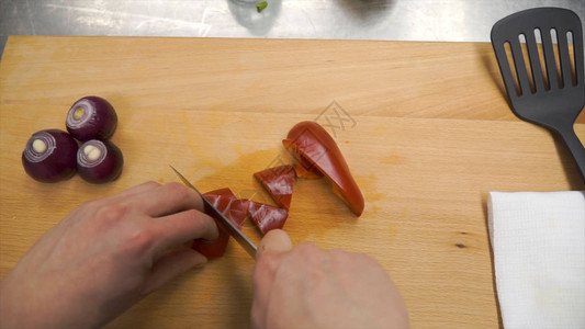 刀在木菜板上切红甜椒夹子在木菜板上用甜椒切芯用刀从红甜椒中取出种子蔬菜的制备图片