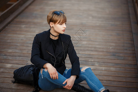 穿着黑色时尚夹克和牛仔裤靴子和皮革时尚包的时尚美丽年轻女坐在户图片