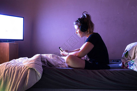 年轻女子晚上在床上看电视上的电影图片