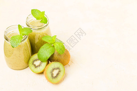 猕猴桃冰沙装饰着新鲜的绿色薄荷叶和黄色柔和背景的生熟切水果图片