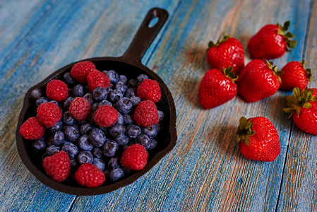 蓝色木制桌上是一块有蓝莓和草莓的铸铁锅图片