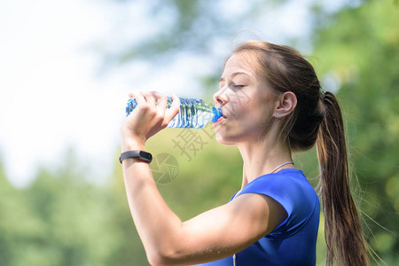 美丽的健康女孩喝着矿泉水从公园的一瓶酒里取出在阳图片