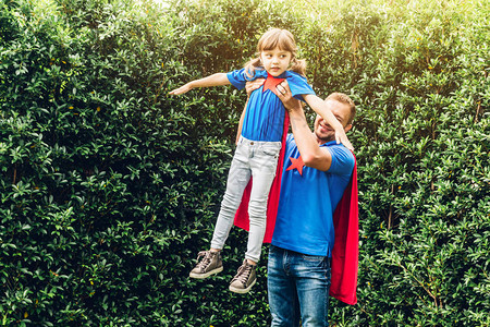 父亲带着小女儿穿着超级英雄服装在户外公园玩乐和玩超级英雄爱家庭图片